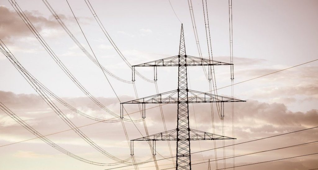 Słup wysokiego napięcia z liniami energetycznymi na tle zachmurzonego nieba – ilustracja do informacji o przerwach w dostawie prądu