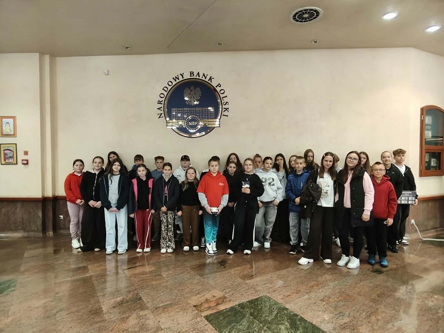 Grupa uczniów SP w Długołęce-Świerkli w holu Narodowego Banku Polskiego we Wrocławiu, pod godłem NBP