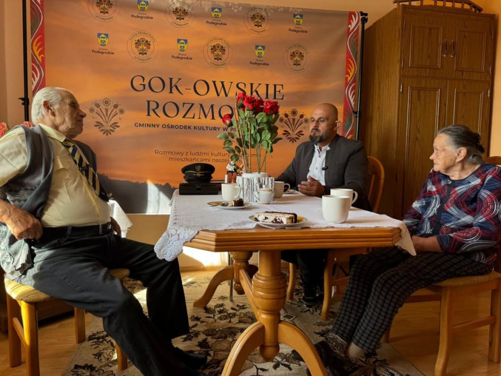 Nagranie pierwszego odcinka „GOK-owskich Rozmów” – rozmowa przy stole z kawą na tle banera Gminnego Ośrodka Kultury w Podegrodziu