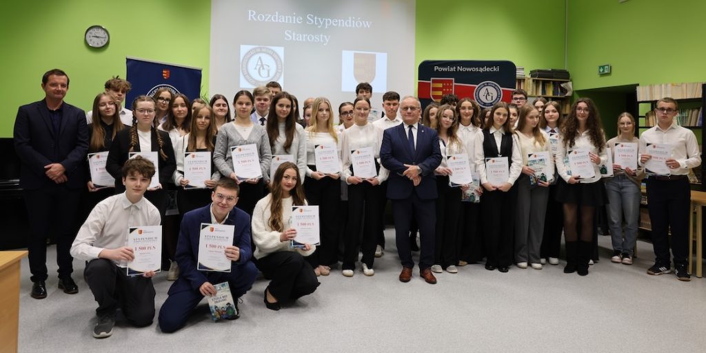Rozdanie stypendiów Starosty Nowosądeckiego w Liceum Ogólnokształcącym im. Artura Grottgera w Grybowie – trzech mężczyzn przy banerze Powiatu Nowosądeckiego
