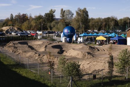 Budowa pumptracka w Świniarsku – ziemne garby toru za ogrodzeniem, w tle namioty festynu i balon z logo Małopolski