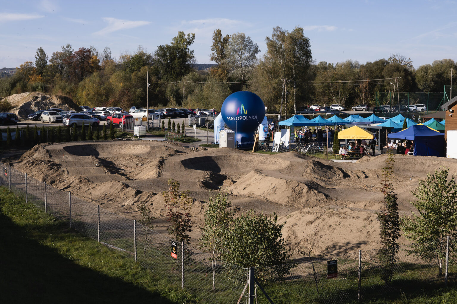Budowa pumptracka w Świniarsku – ziemne garby toru za ogrodzeniem, w tle namioty festynu i balon z logo Małopolski